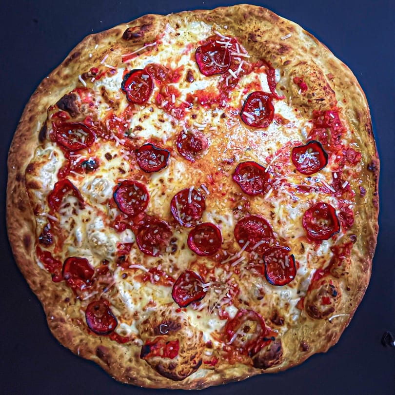 A whole pepperoni pizza with melted cheese and a golden crust on a dark surface.